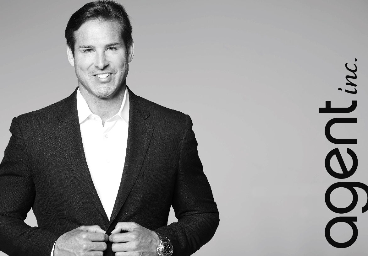Black and white portrait of a smiling professional real estate agent, with the AGENT INC. logo vertically positioned to the right.