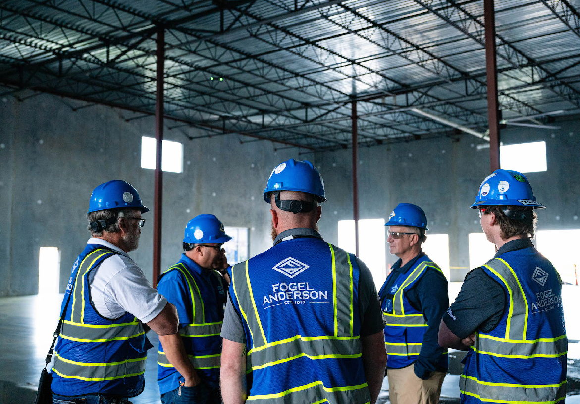 The Fogel Anderson construction management team conducting a site walk-through inside a commercial building frame, wearing branded safety gear.