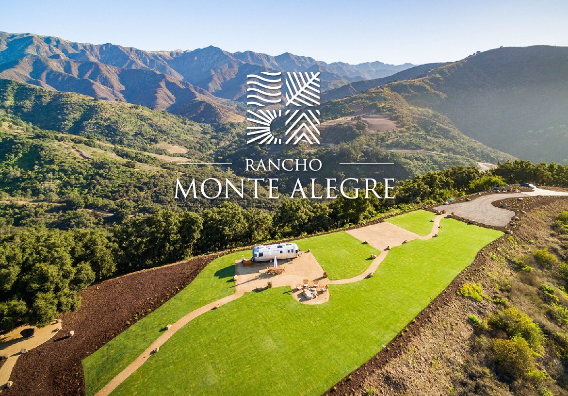 Aerial drone view of a green home site at Rancho Monte Alegre, displayed next to the brand's logo on blue and green color blocks representing the sky and earth.