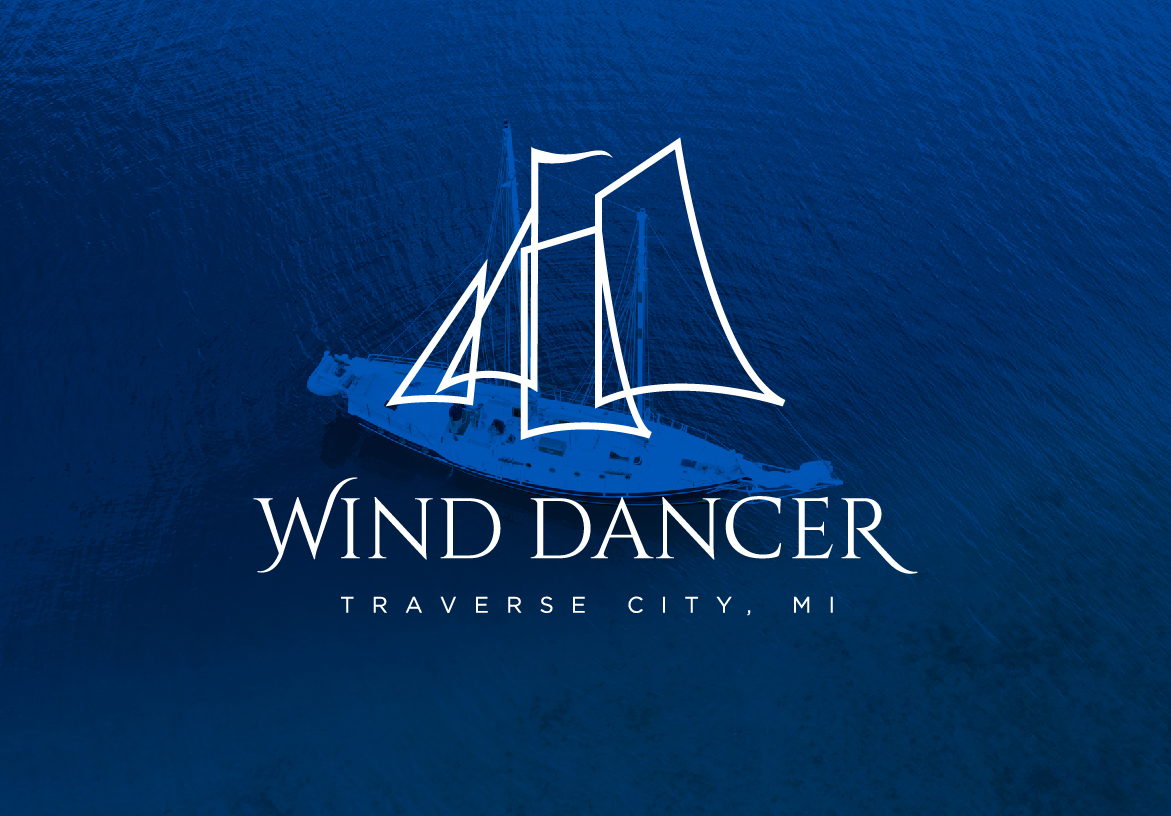 Wind Dancer logo in white overlaying a deep blue image of Grand Traverse Bay water, emphasizing the connection to the lake and sailing.