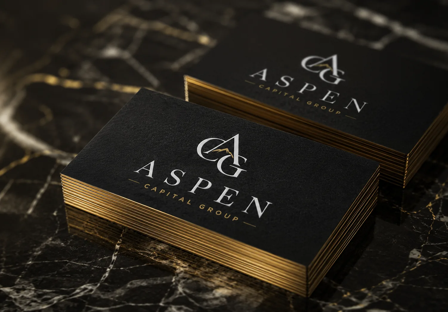 Stack of black Aspen Capital Group business cards with gold edges on a marble surface