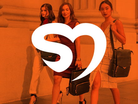 White abstract heart logo with a S + M letter shape for SheMedia overlaid on a vibrant orange-tinted photo of fashionable women walking in a city, representing female empowerment.