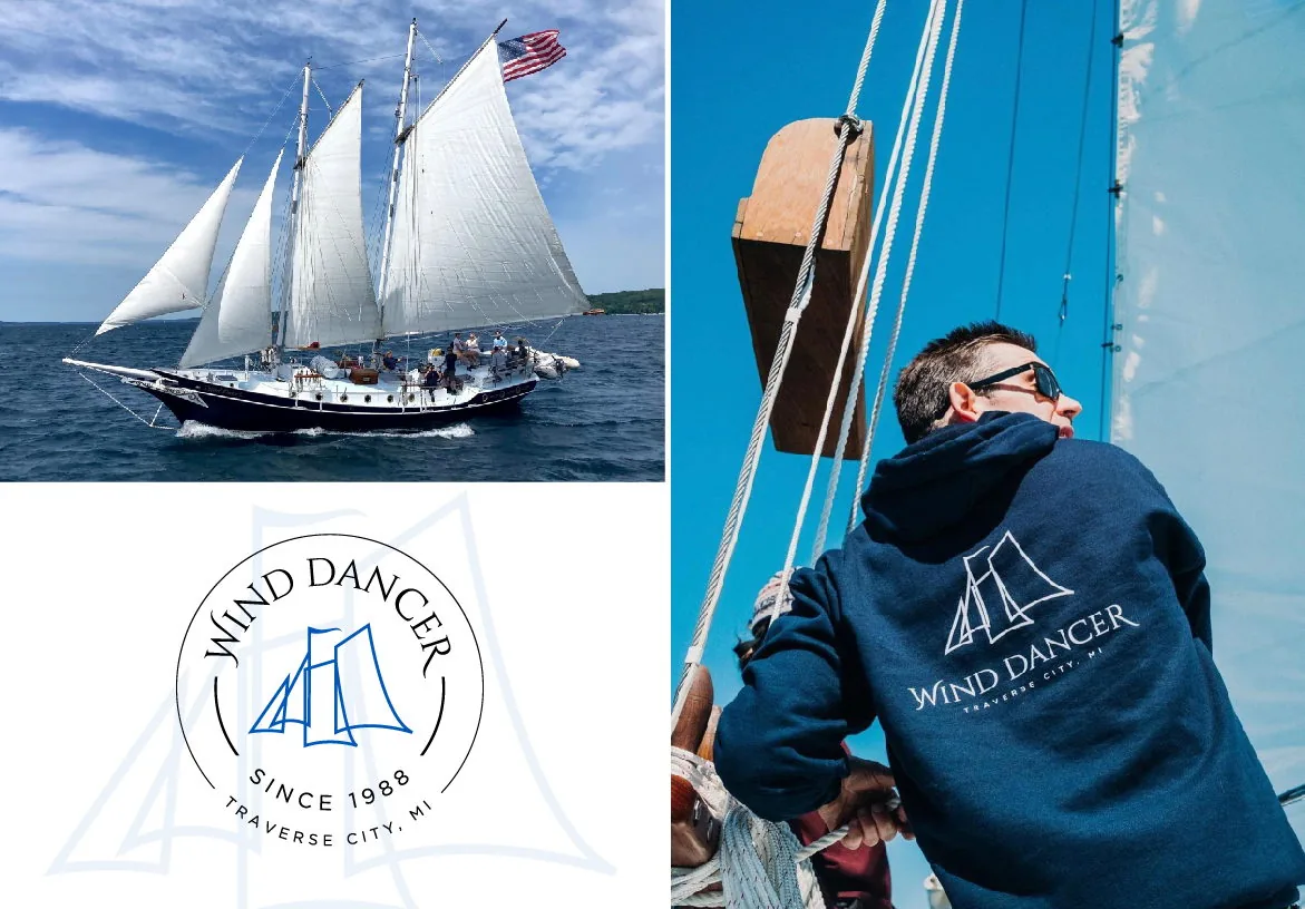The Wind Dancer schooner with sails fully raised and a crew member wearing a branded navy blue hoodie