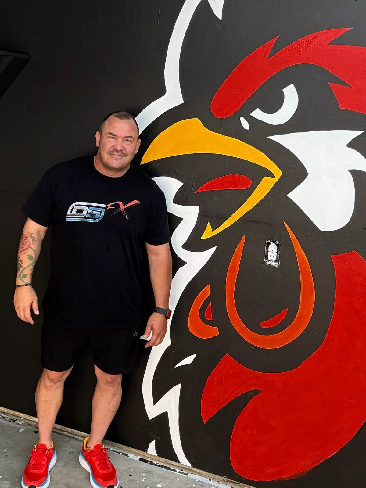 Person standing beside the Wake Up Sports rooster mural for scale
